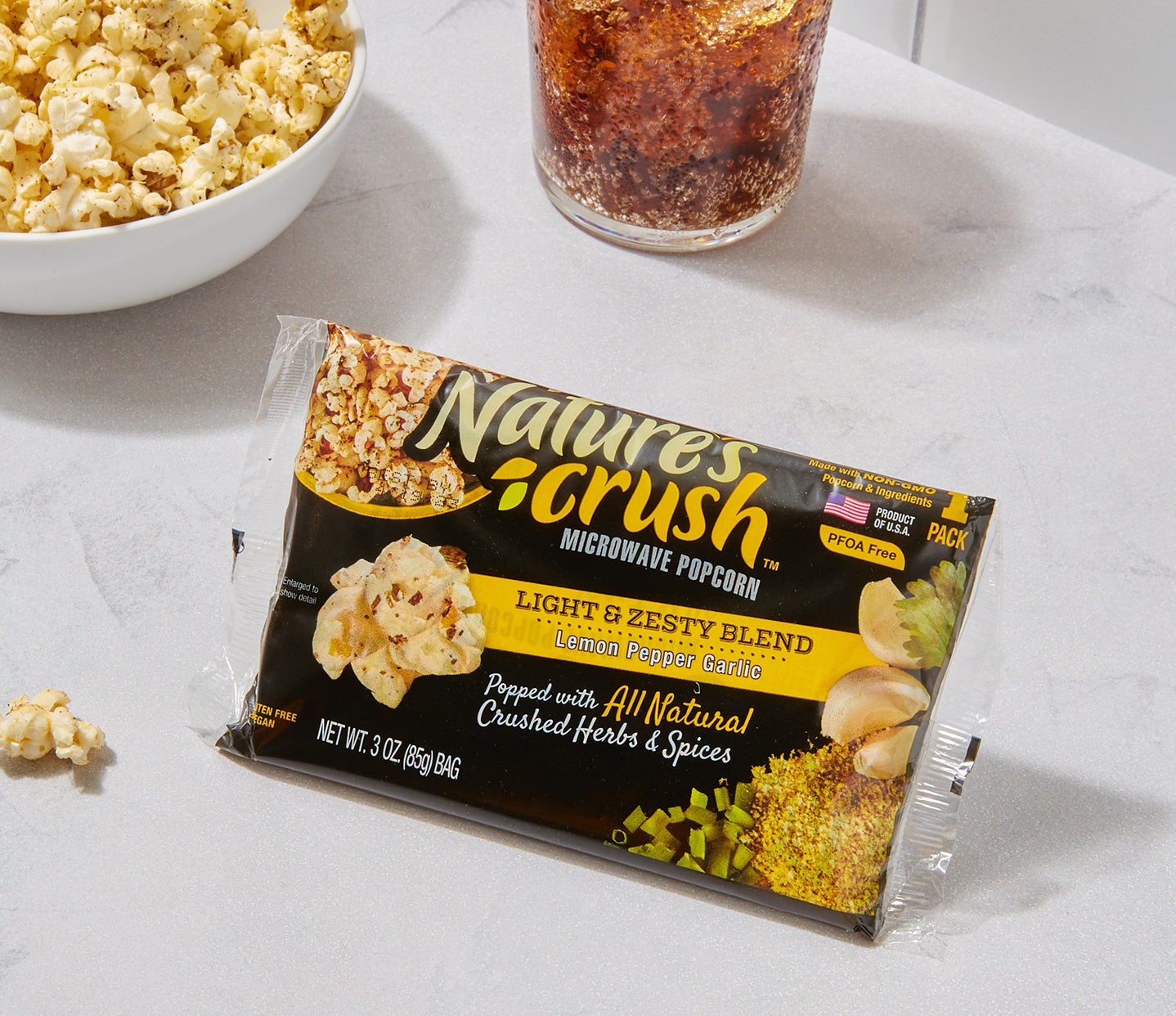 Lemon Pepper Garlic Popcorn bag with bowl of popcorn and glass of soda in background on a marble surface.