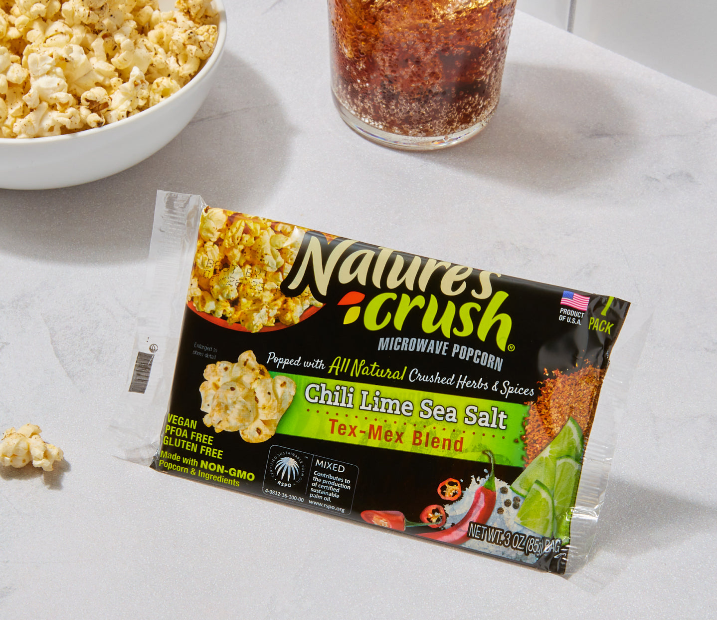 Tex-Mex popcorn bag with bowl of popcorn and glass of soda in background on a marble surface.