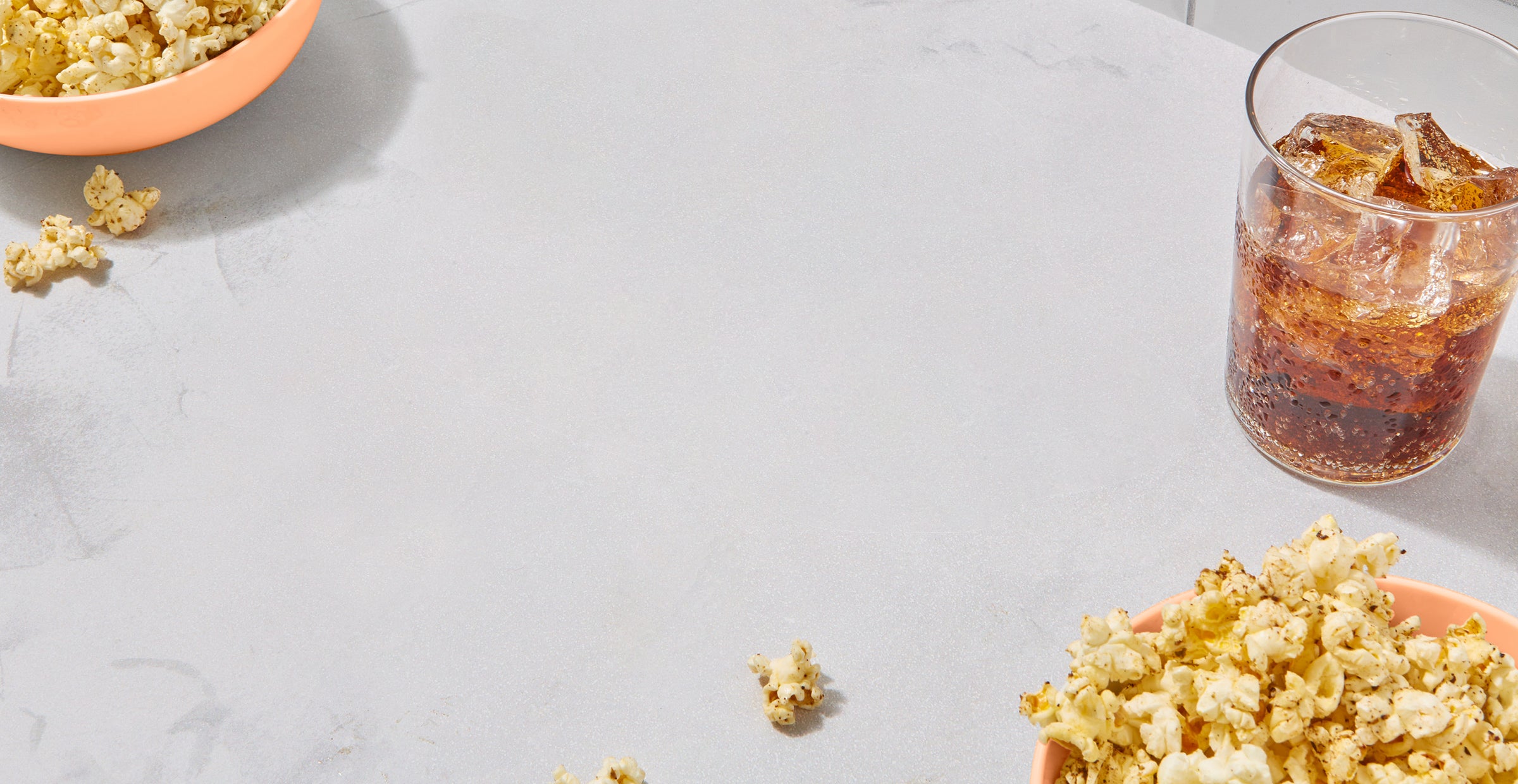 Bowls of popcorn and a soda on marble surface.