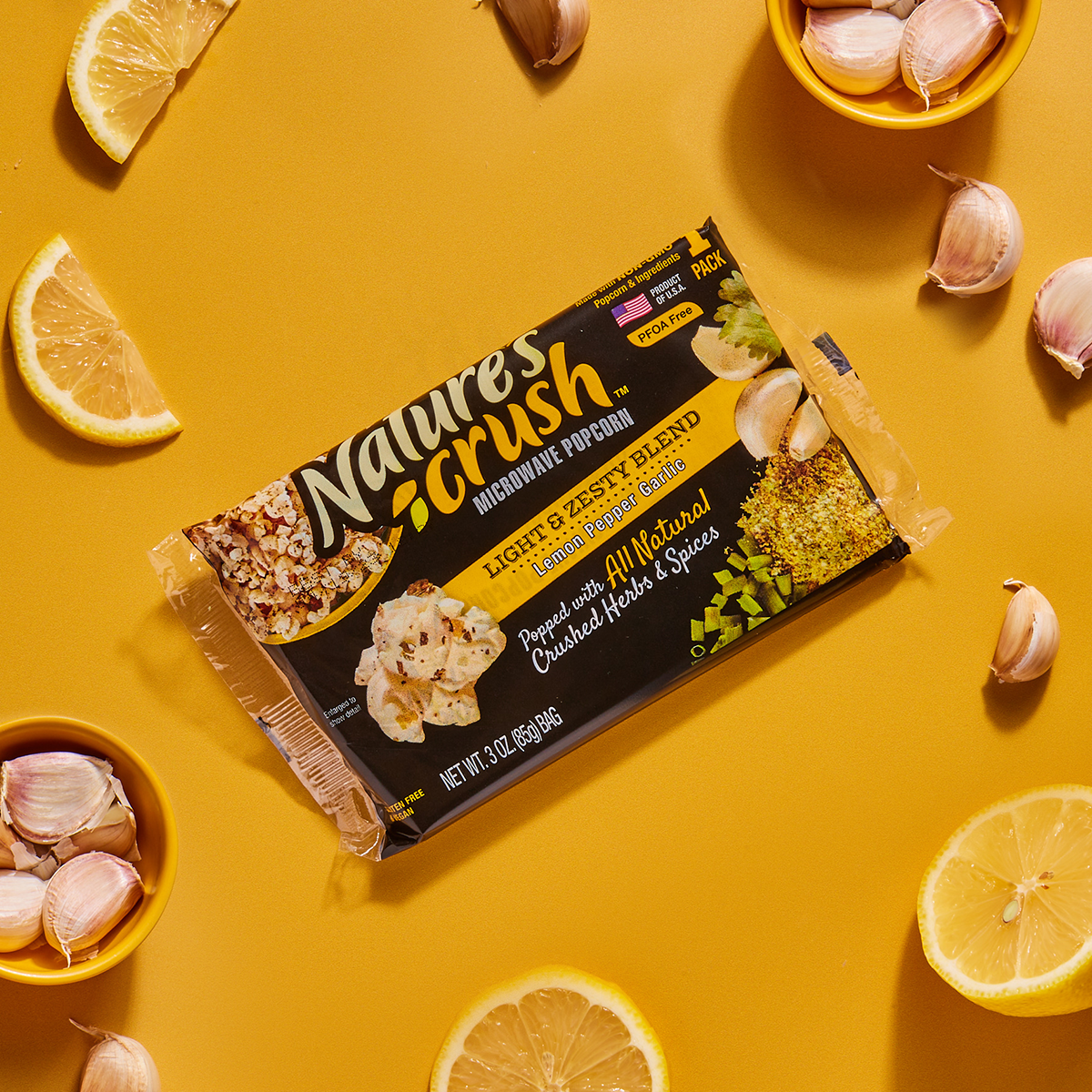 Bag of Light & Zesty Popcorn surrounded by scattered lemons and garlic on yellow surface.