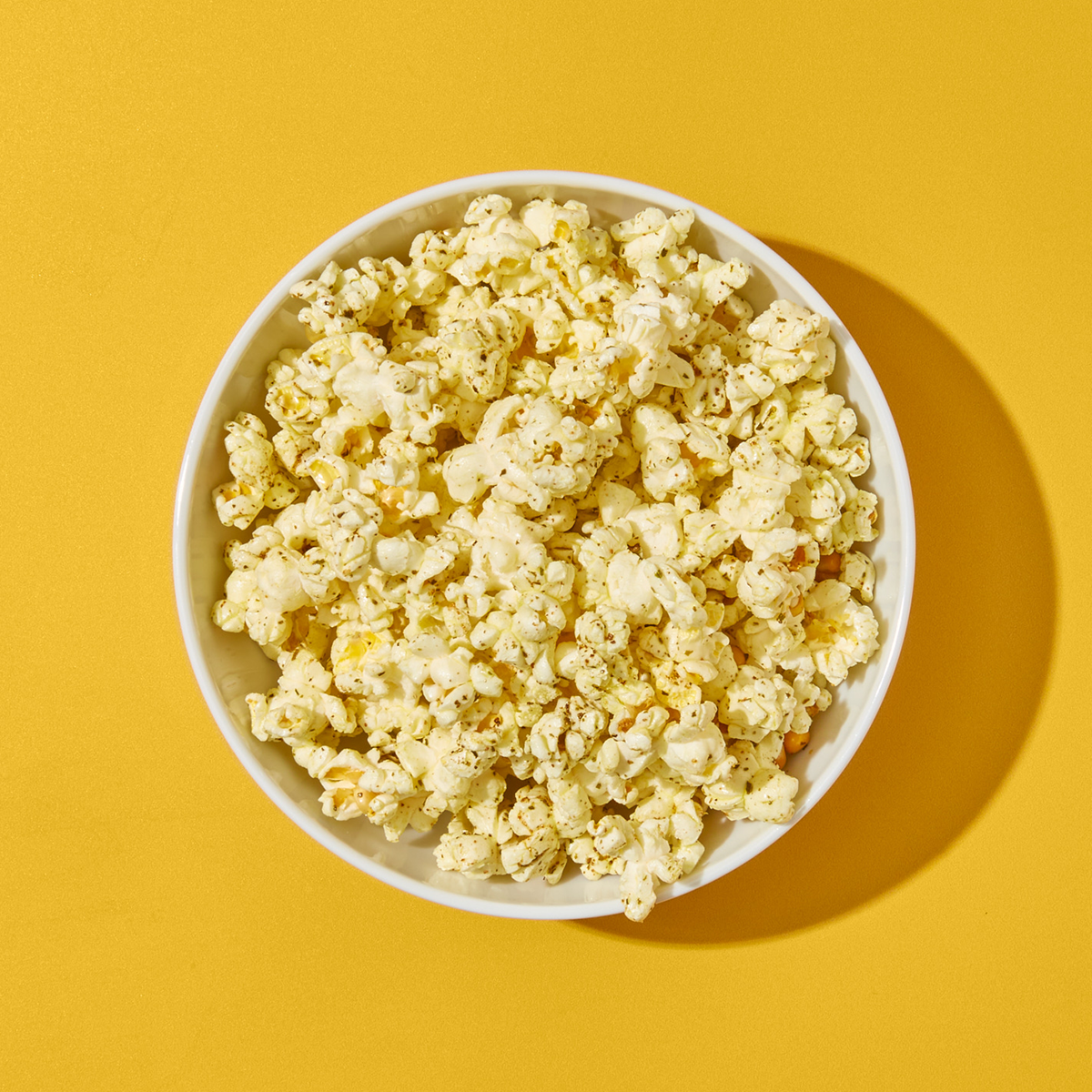 Bowl of light & Zesty Popcorn on yellow surface.